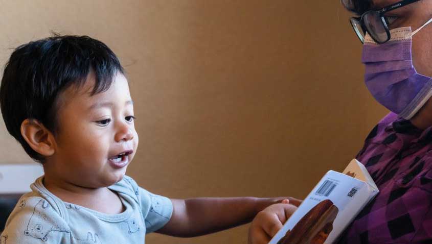 Toddler reaching toward a picture book held by a caregiver